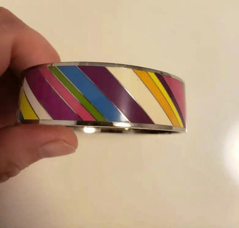 A hand holding a colorful striped Coach bangle bracelet against a plain light background.