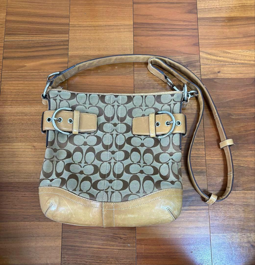 Brown COACH canvas shoulder bag with repeating 'C' monogram and tan leather trim laid on a wooden floor.