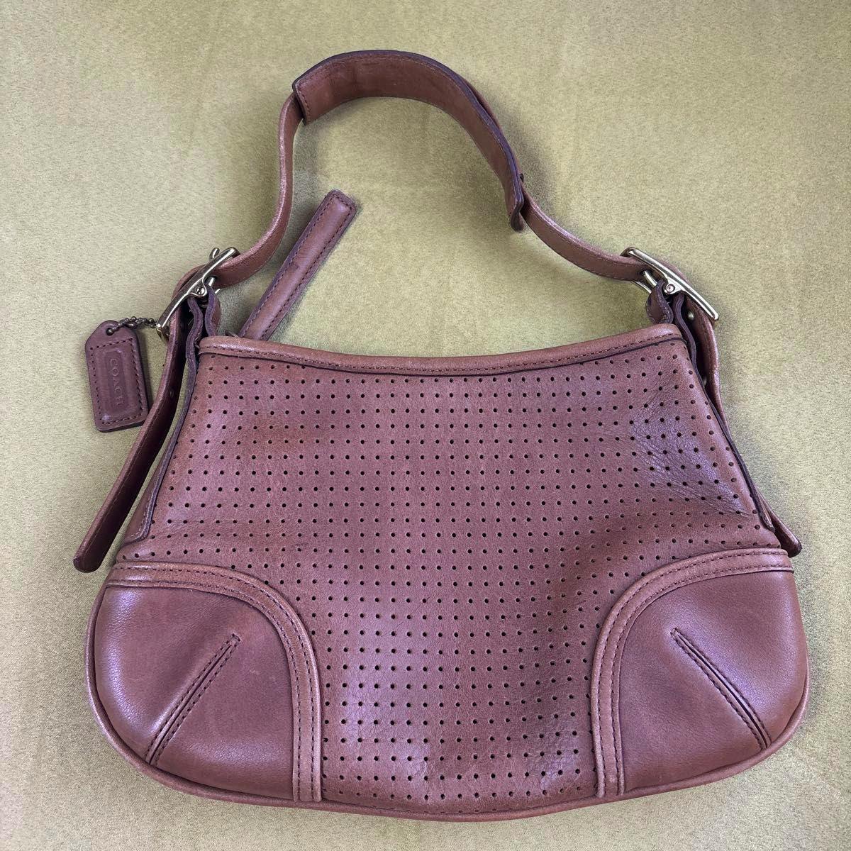Brown Coach leather shoulder handbag with a perforated front panel and short strap laid flat on a green background.