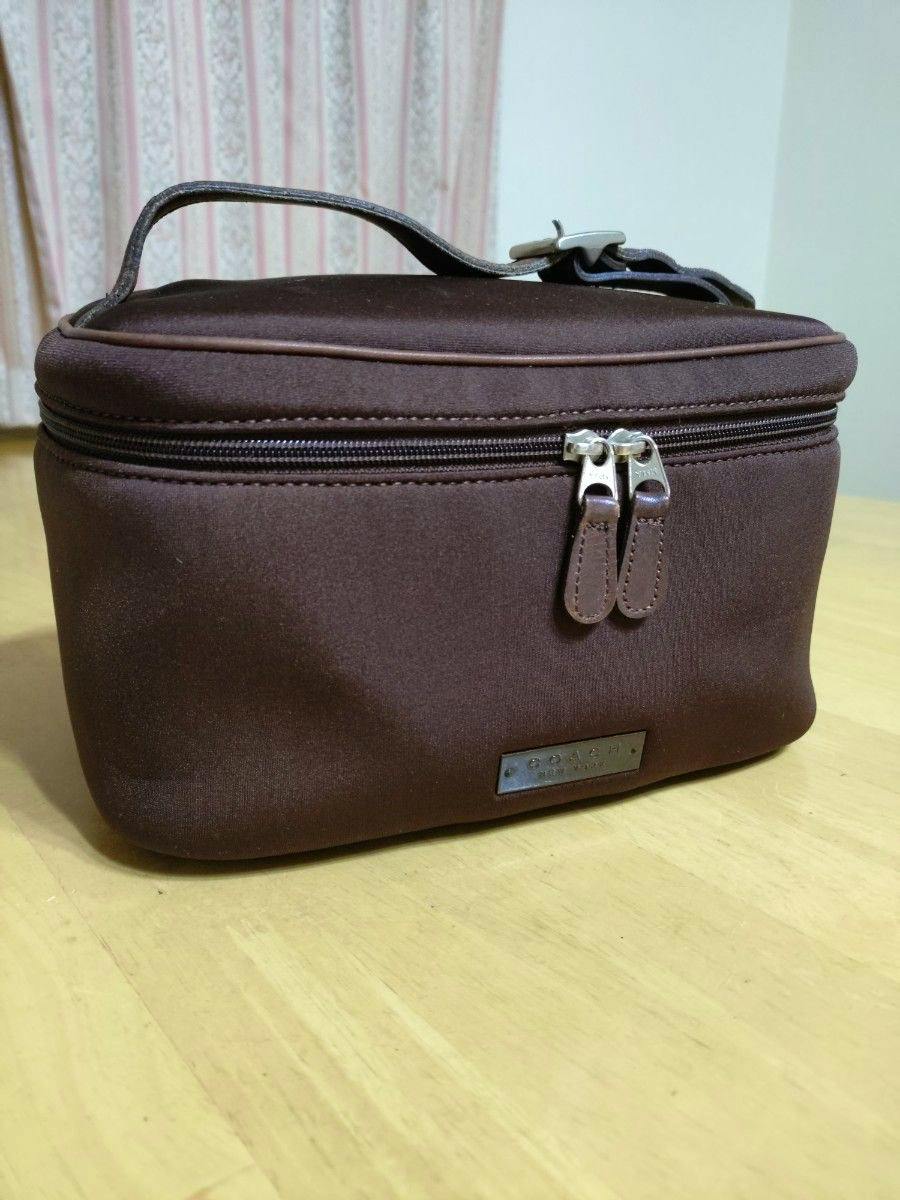 Brown COACH nylon vanity pouch with a top handle and double-zip closure shown on a wooden surface.