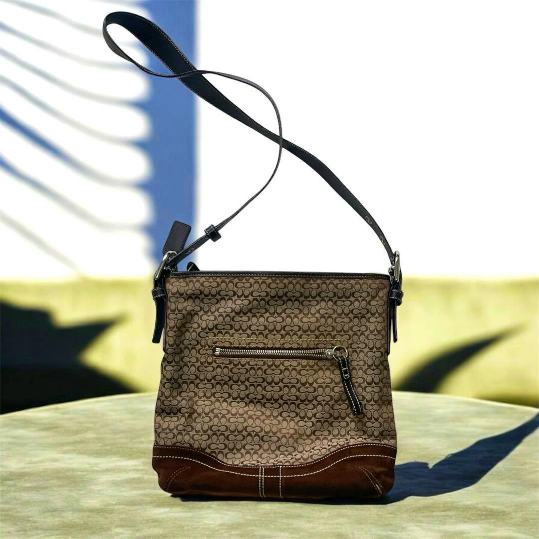 Brown Coach shoulder bag with signature monogram canvas, brown suede bottom, a front zip pocket, and an adjustable leather strap displayed against a light background.