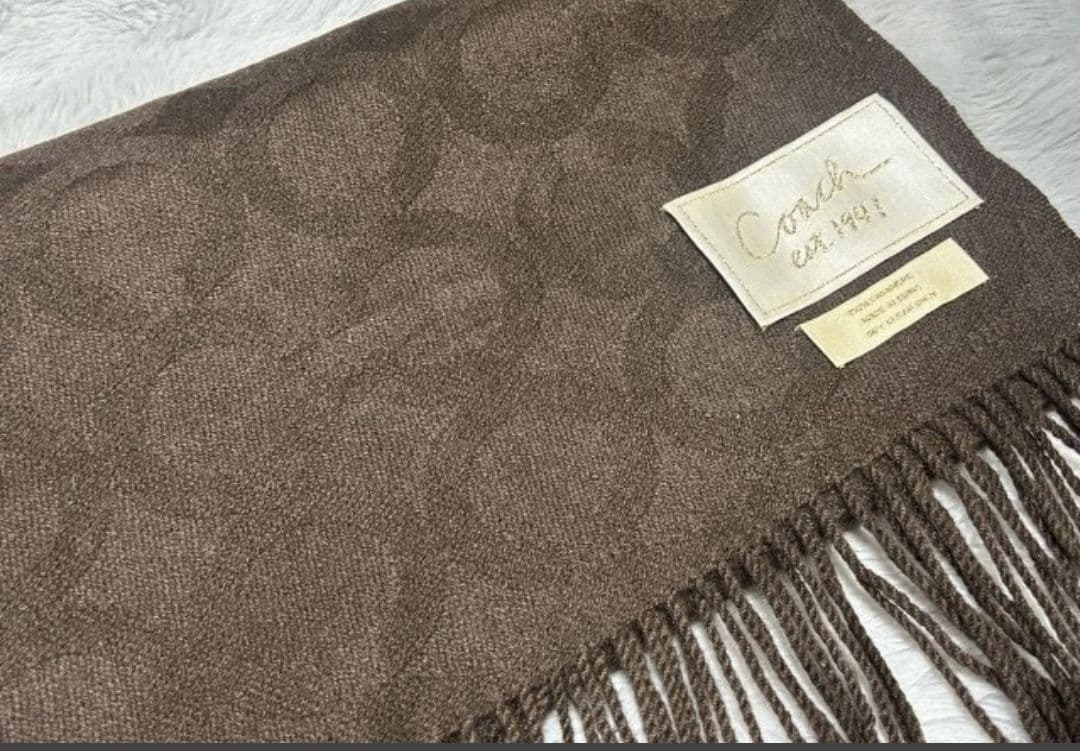 Brown Coach muffler with fringed ends, a fabric Coach label, and signature monogram pattern.
