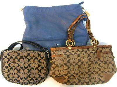 Three Coach bags arranged together: a light blue bag in back and two brown signature canvas Coach bags in front.