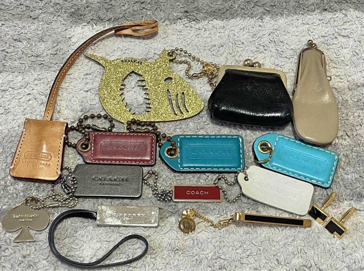 Multiple leather Coach key tags, small coin purses, metal charms, a gold tie clip and cufflinks arranged on a cloth background.