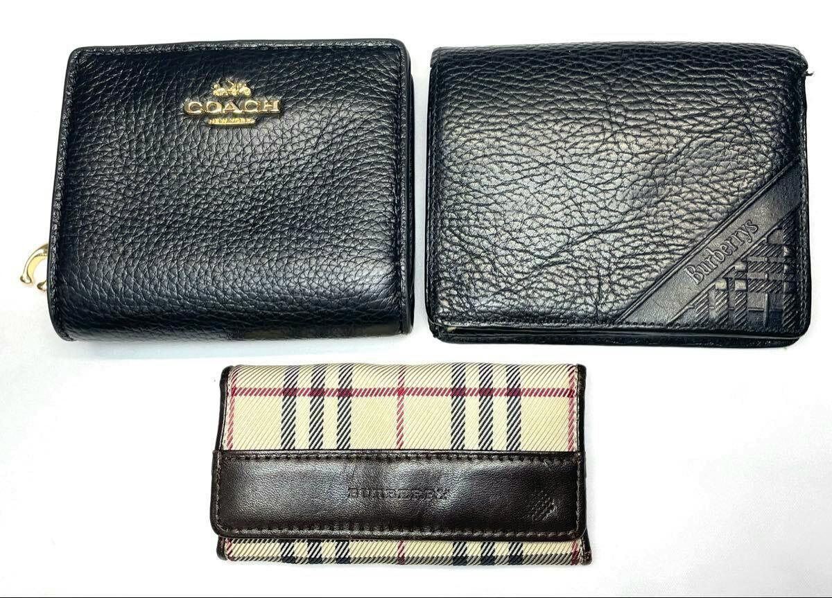 Two black leather wallets and a Burberry check key case arranged on a white background.