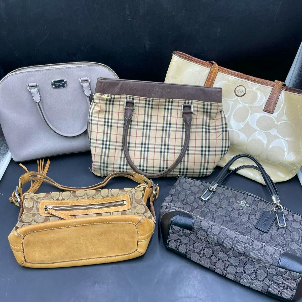 Multiple canvas and leather shoulder and tote bags, including a Coach signature bag and other patterned bags, arranged on a dark surface.