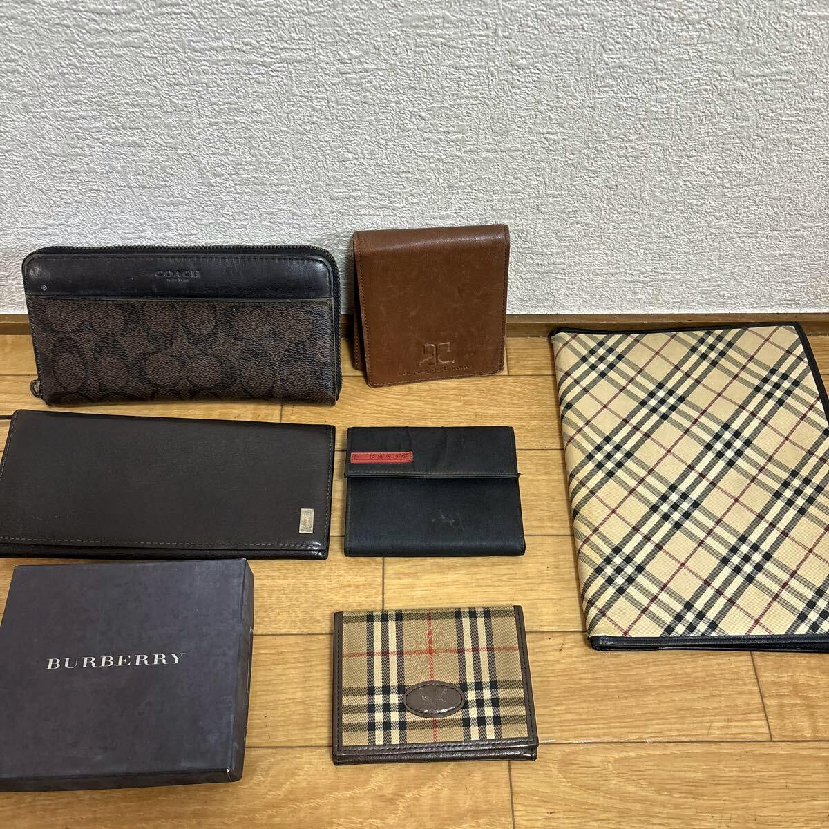 Multiple wallets and a Burberry check folder and box arranged on a wooden floor.