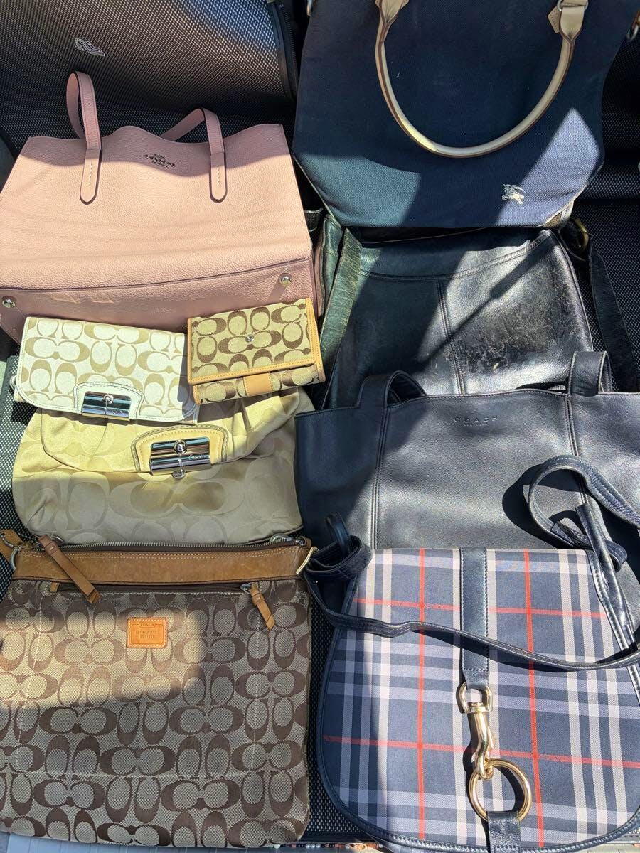 Multiple canvas and leather bags and wallets including Coach and Burberrys signature styles arranged together.
