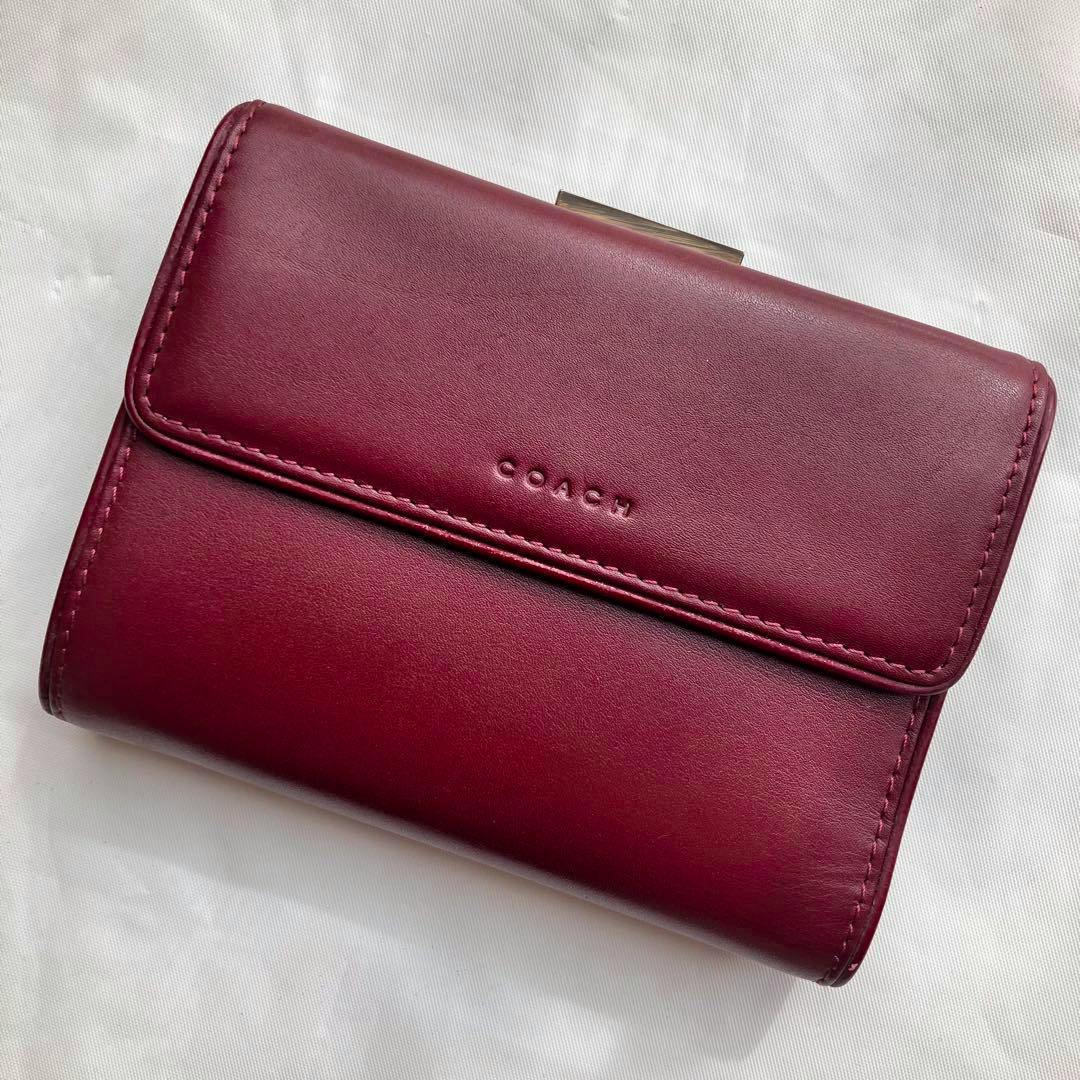 Front view of a bordeaux COACH bi-fold leather wallet showing the embossed COACH logo and a metal kiss-lock clasp.
