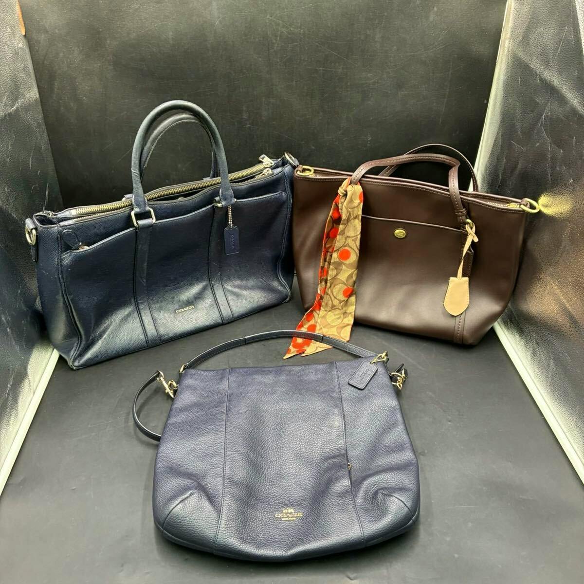 Three COACH cow leather bags (two dark blue and one brown) arranged on a black background.