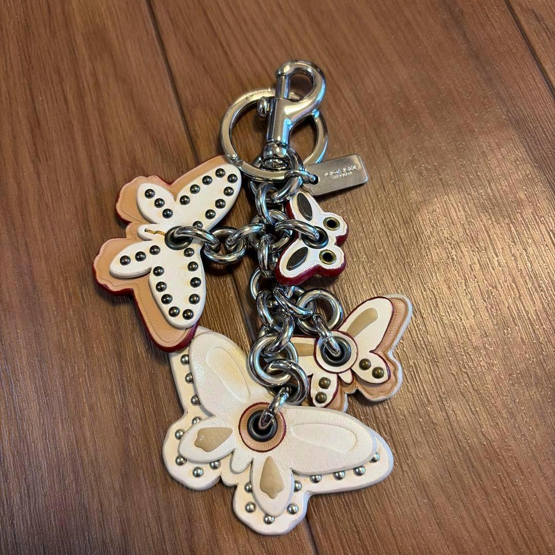 Leather COACH butterfly charm keychain with multiple butterfly charms and a metal clasp on a wooden surface.