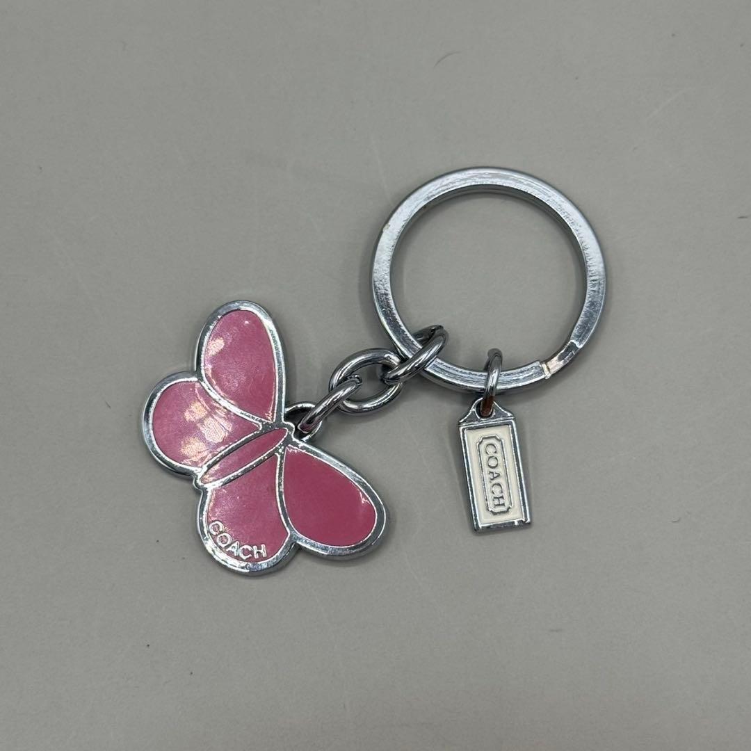 Silver keychain with a pink butterfly charm and a small Coach tag on a key ring.