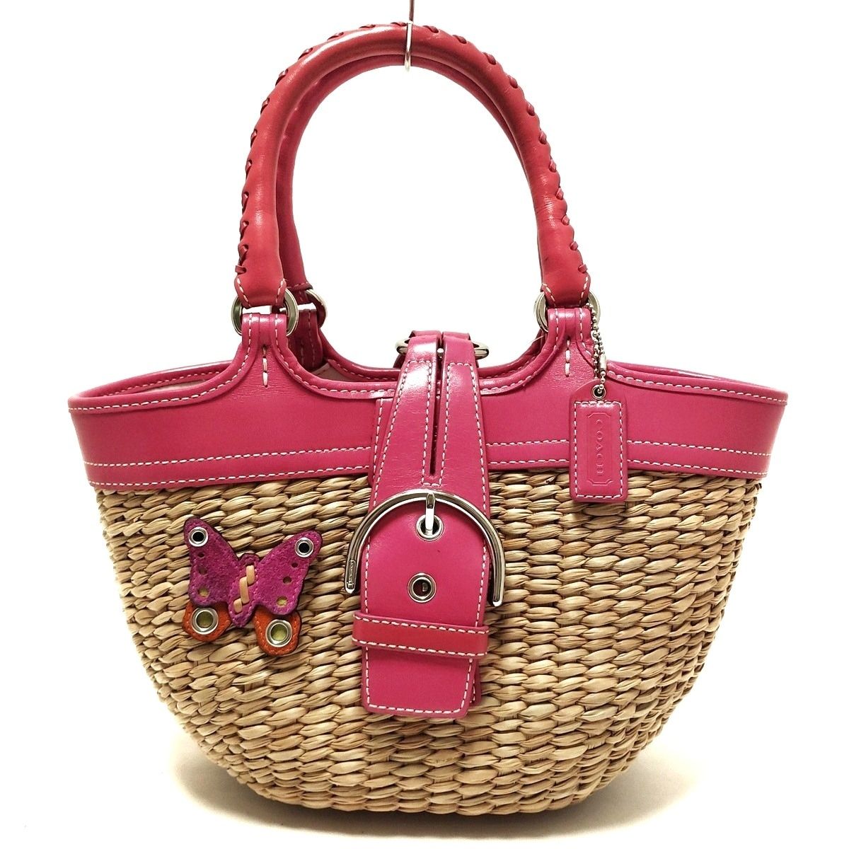 Front view of the beige woven COACH basket handbag with pink leather trim, handles, buckle strap, and a butterfly decoration.