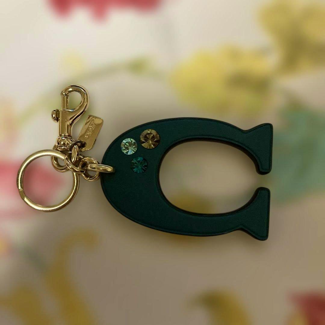 COACH C-logo keychain charm in dark green with three small crystals and gold-tone hardware.