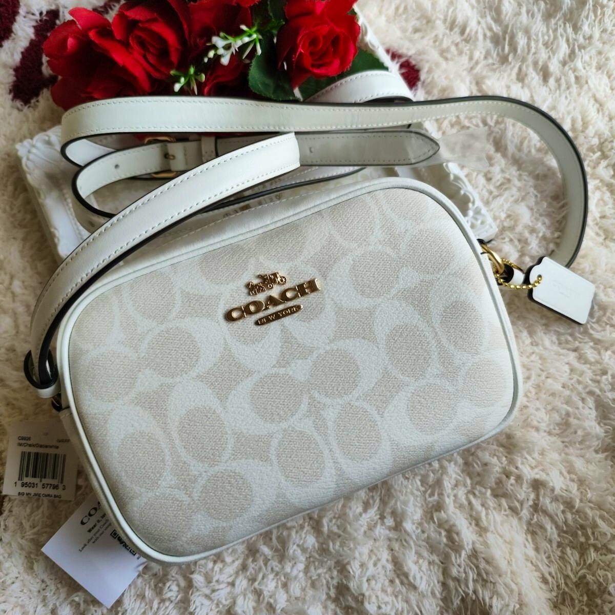 White COACH signature-pattern mini shoulder bag with gold logo and strap shown on a textured surface.