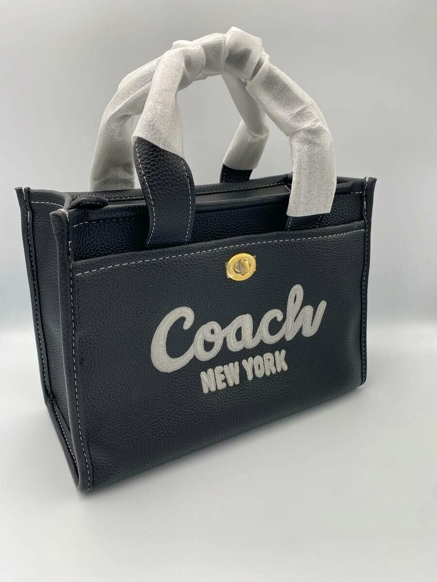 Black Coach leather bag with white embroidered "Coach New York" logo and wrapped top handles.