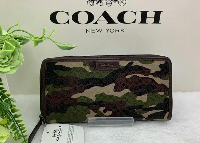 Front view of a COACH camouflage long canvas zip-around wallet displayed in front of a COACH box.