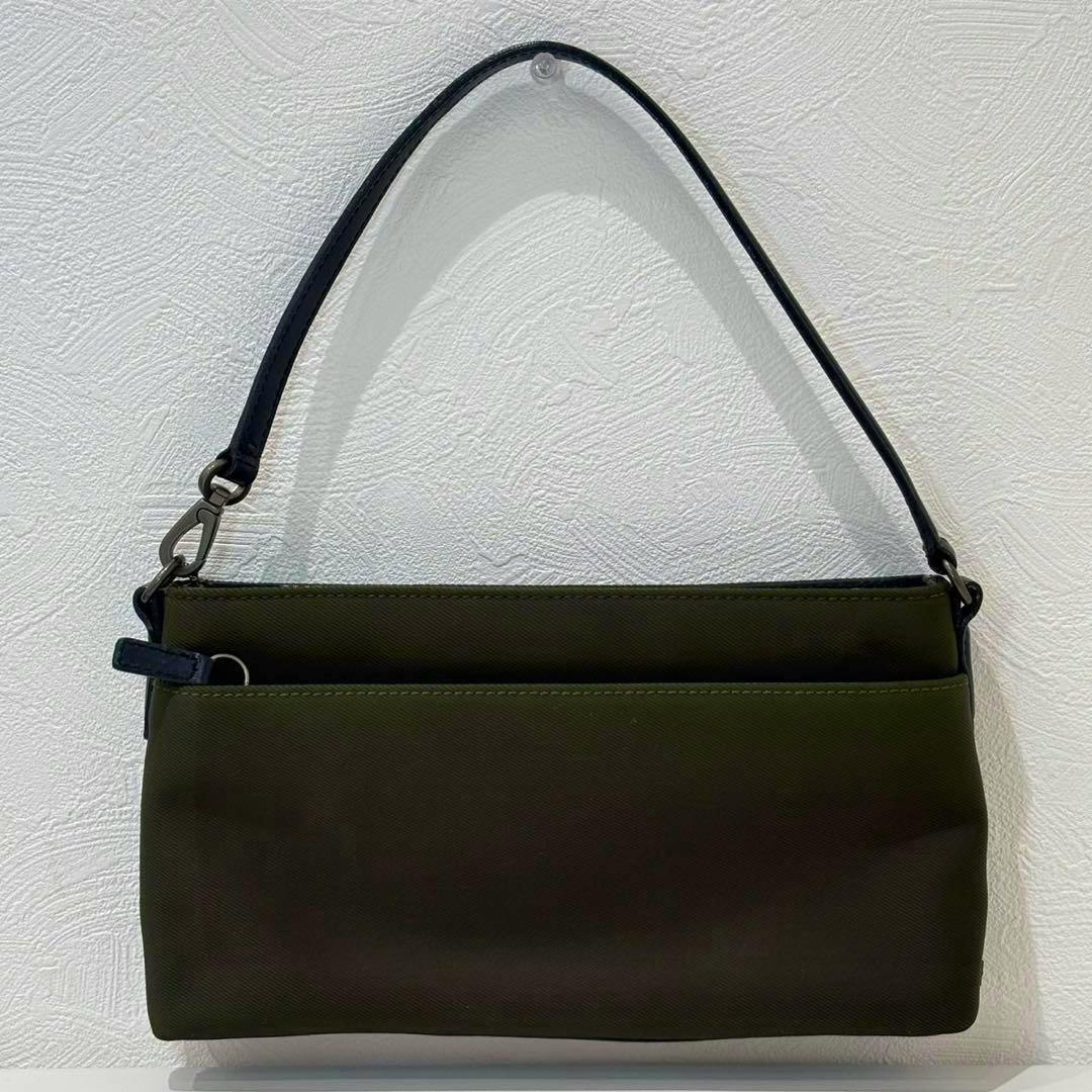 Olive-green canvas COACH accessory pouch handbag with a short black shoulder strap hanging against a white textured wall.
