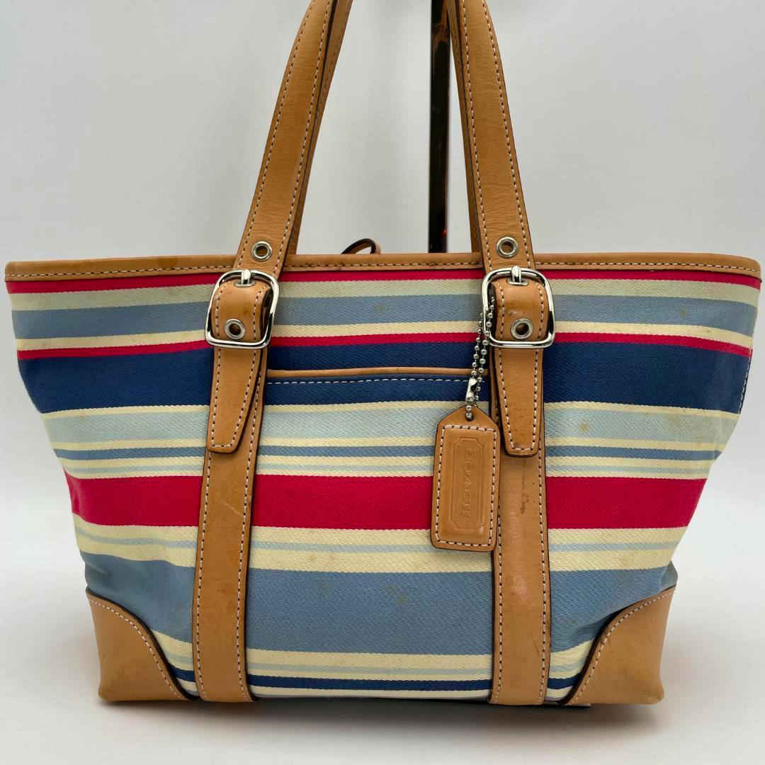Front view of a Coach canvas handbag with blue, red, and cream horizontal stripes and tan leather handles and trim.