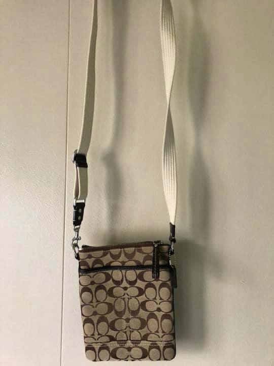 Canvas Coach crossbody bag with brown signature monogram pattern and white adjustable strap hanging on a wall.