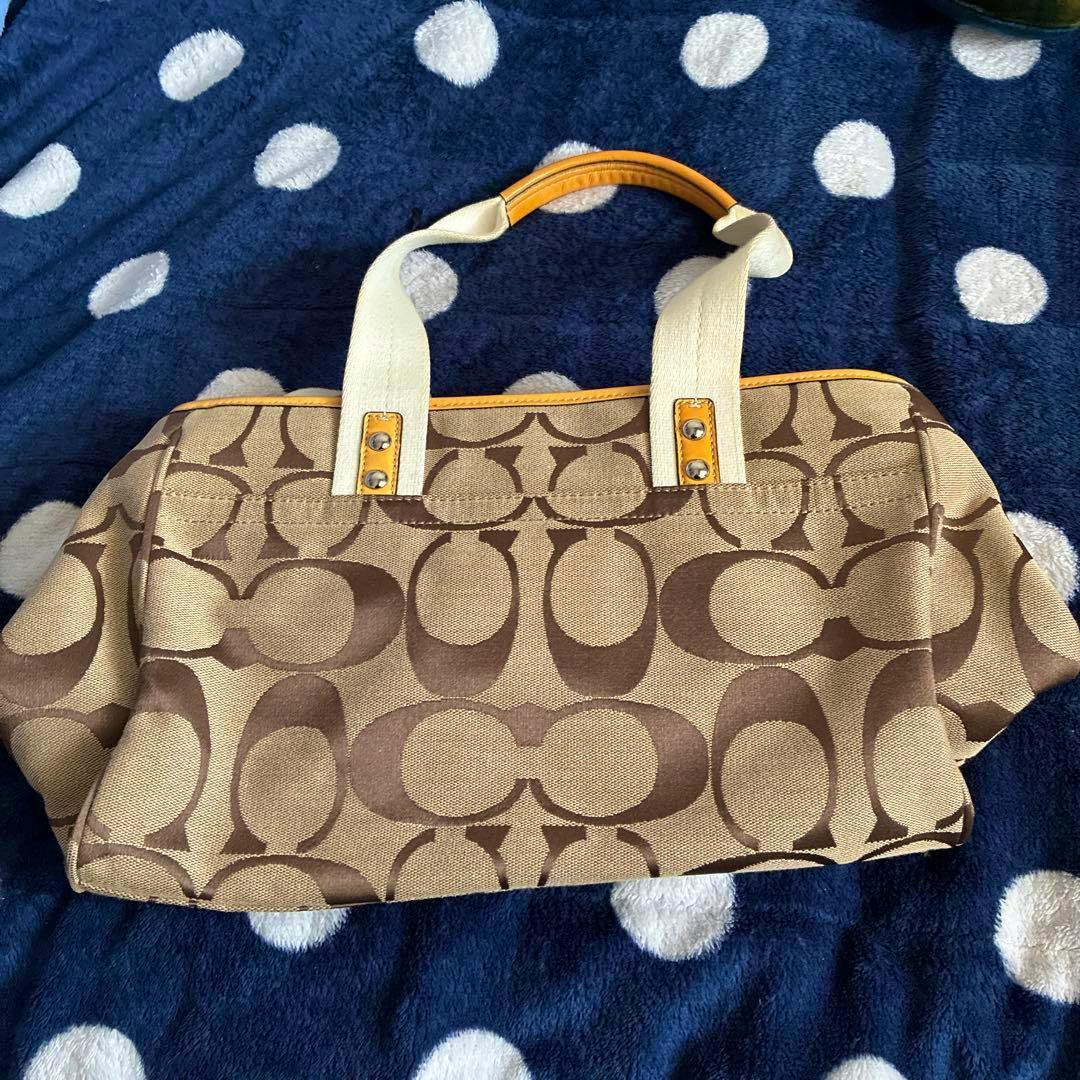 Beige and brown Coach canvas bag with signature 'C' pattern and cream handles on a blue polka-dot blanket.