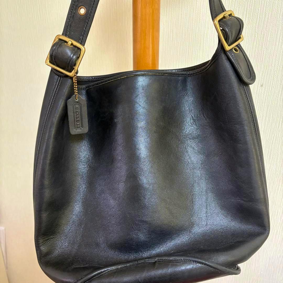 Black COACH bag hanging on a wooden stand showing the front and strap details.