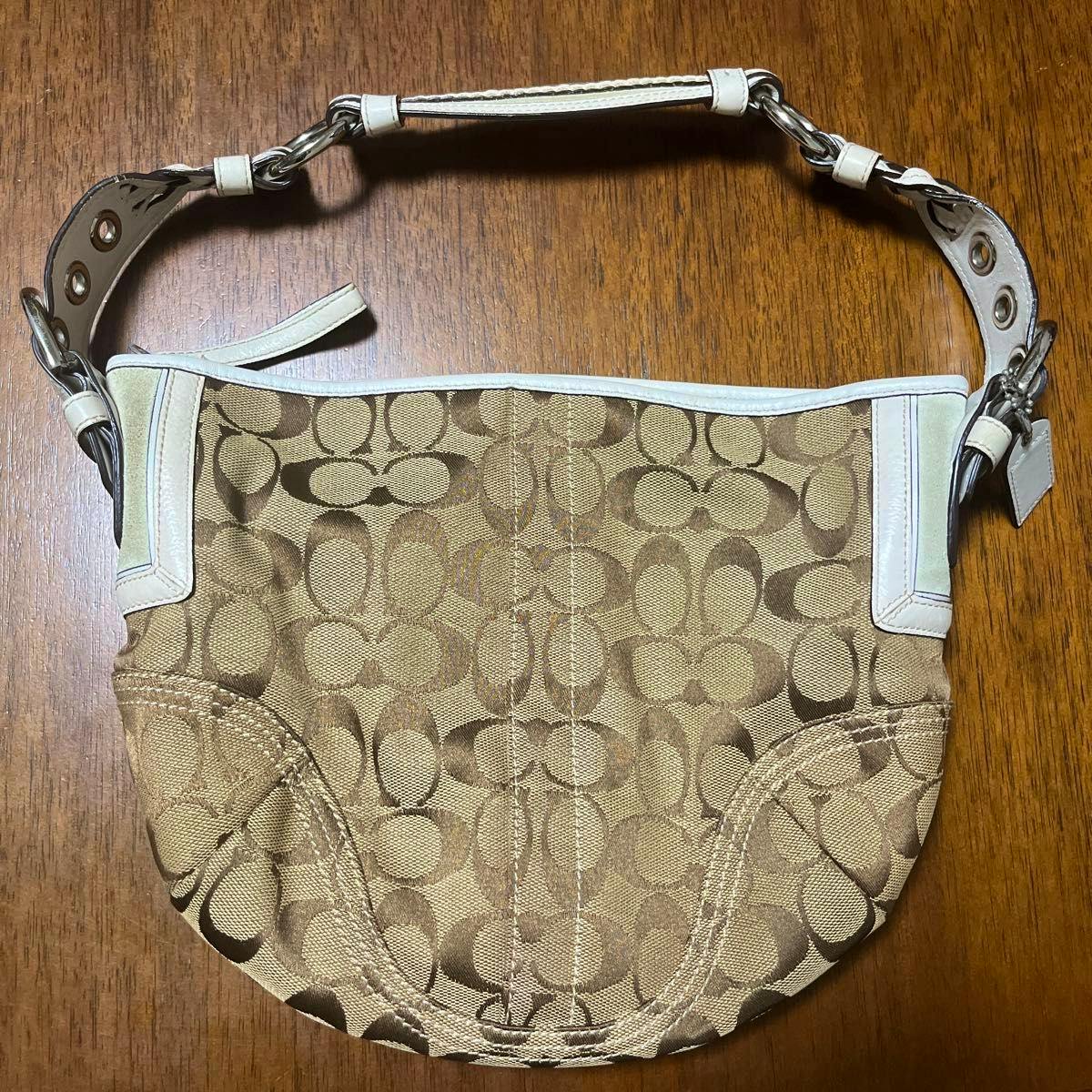 Coach canvas bag with brown signature "C" print and white leather strap and trim lying flat on a wooden surface.