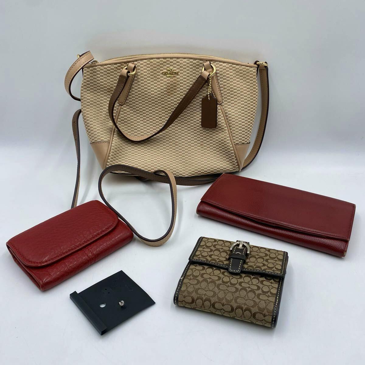 A cream woven Coach handbag with two red leather wallets, a Coach monogram wallet, and a single earring displayed on a white background.