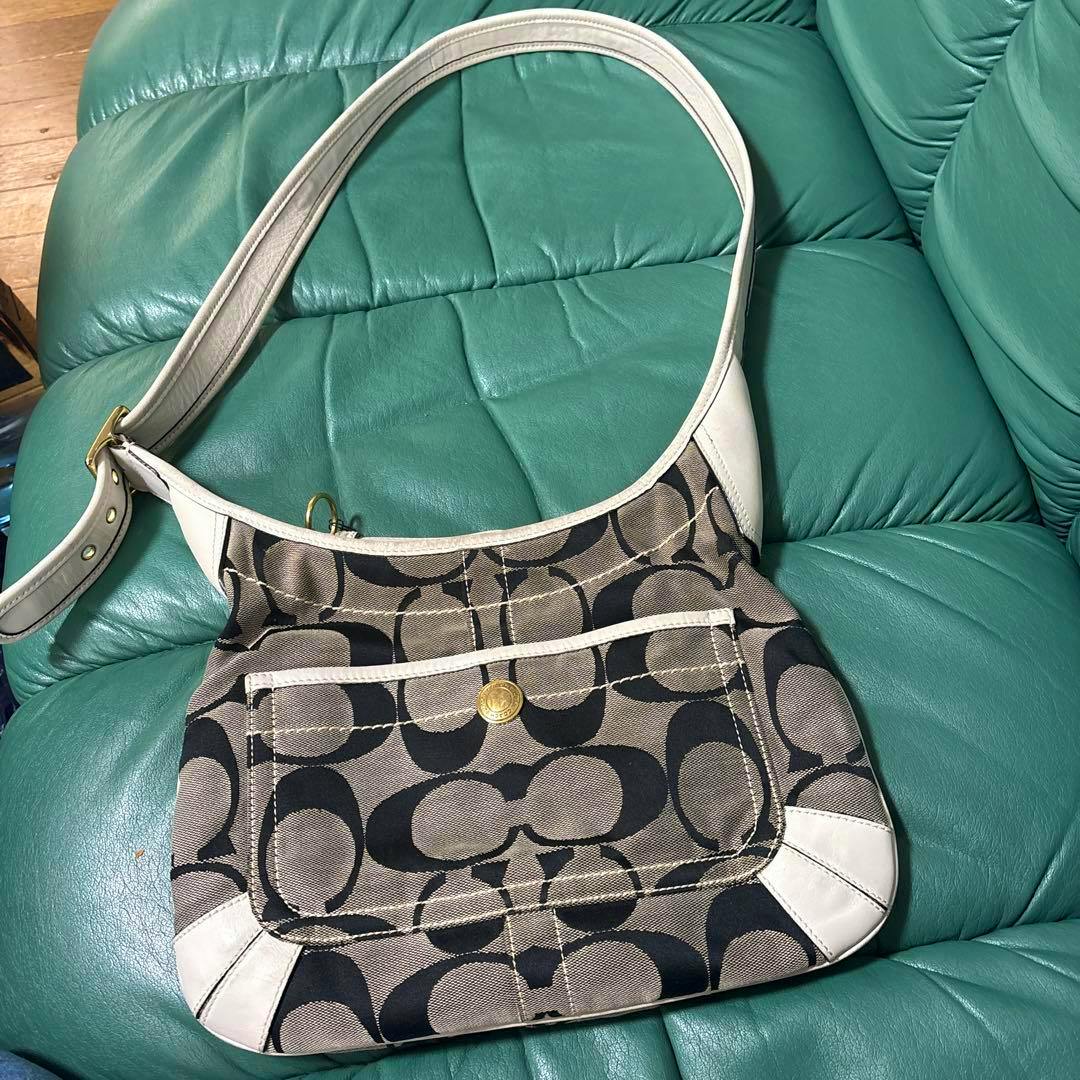 Canvas Coach shoulder bag with brown and black signature 'C' pattern and white leather trim lying on a green sofa.
