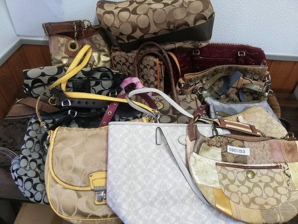 A collection of multiple used COACH handbags and shoulder bags in various patterns and colors arranged on a table.