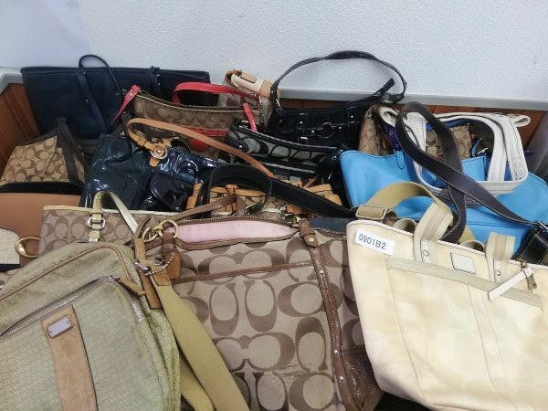 Multiple Coach bags and purses piled together showing various styles and colors.