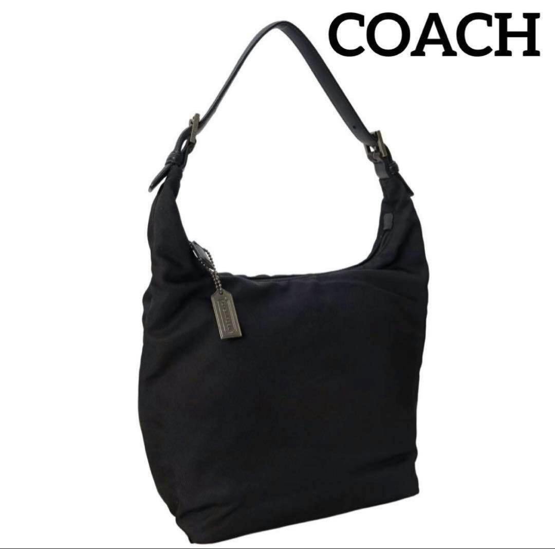 Black Coach canvas shoulder handbag with a single strap and metal Coach tag on a white background.