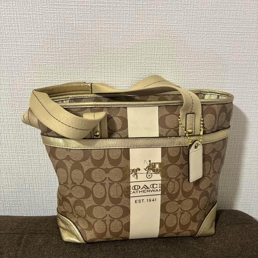 Coach canvas handbag with brown signature 'C' pattern, a cream center stripe, gold trim, and top handles.