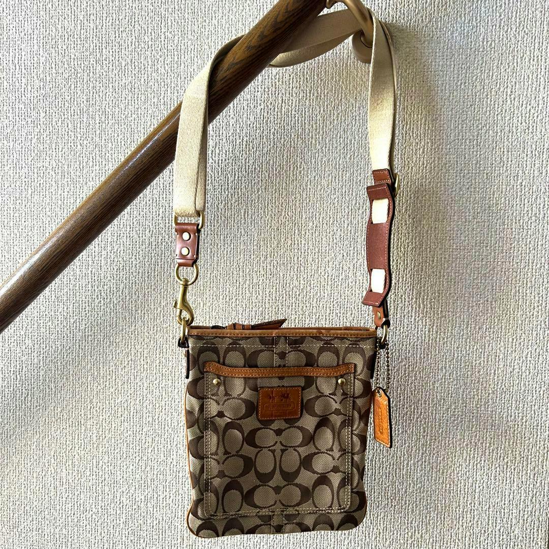 Front view of a COACH canvas shoulder bag with signature C pattern, leather trim, front pocket, leather tag, and an adjustable shoulder strap.