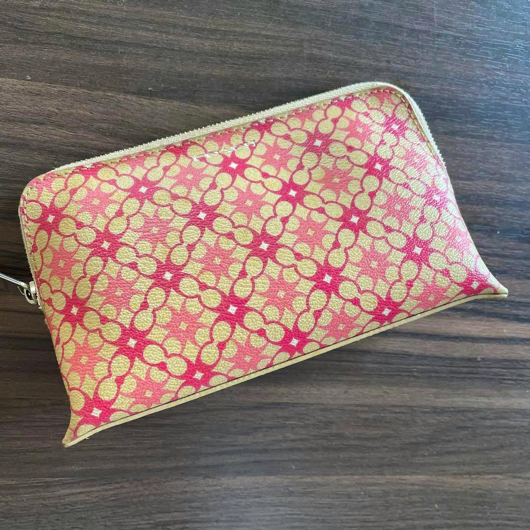 Coach canvas pouch with a pink and gold repeating pattern laid on a wooden surface.