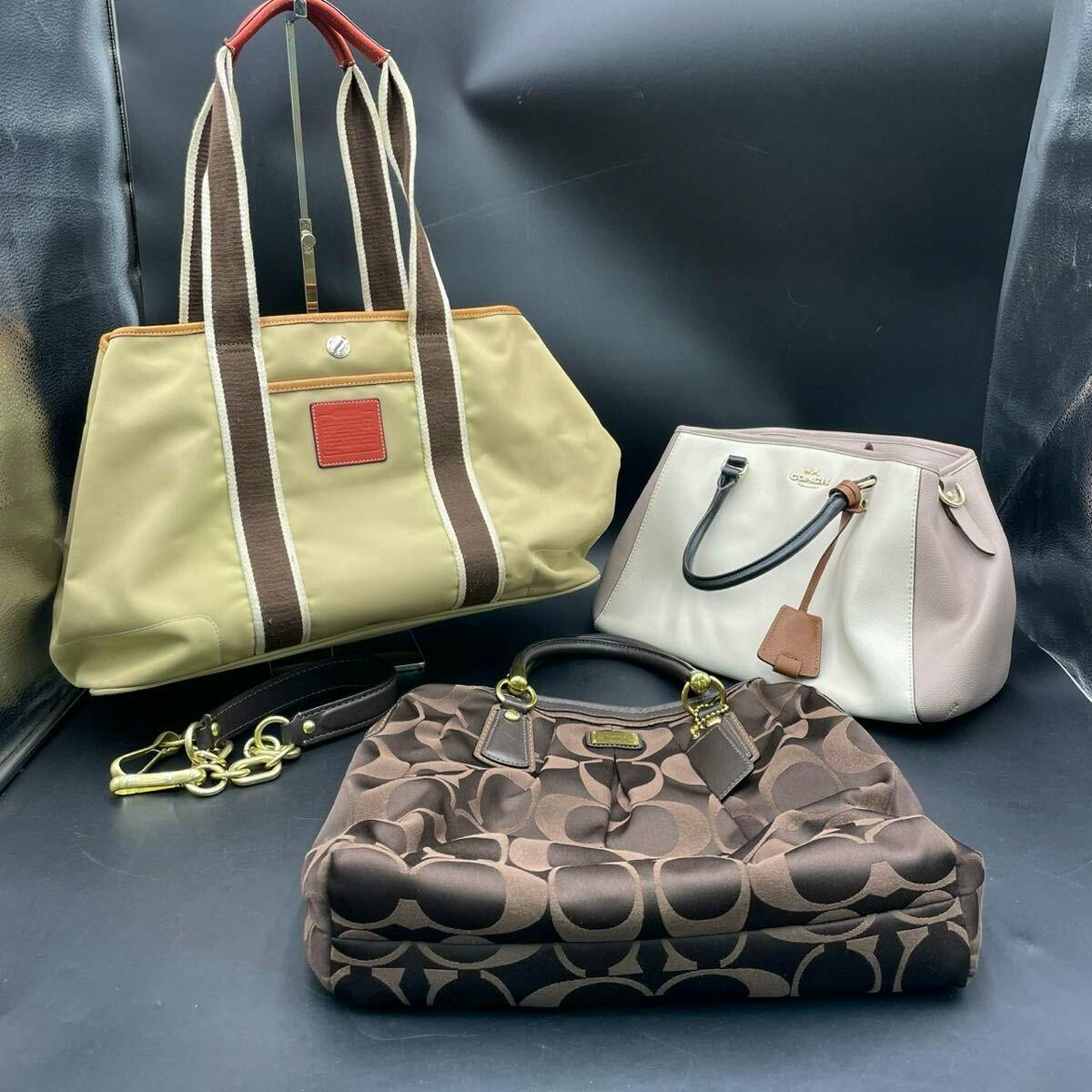 Three Coach bags displayed on a dark background: a beige tote with brown-striped straps, a pale pink/white satchel, and a brown Coach monogram shoulder bag.