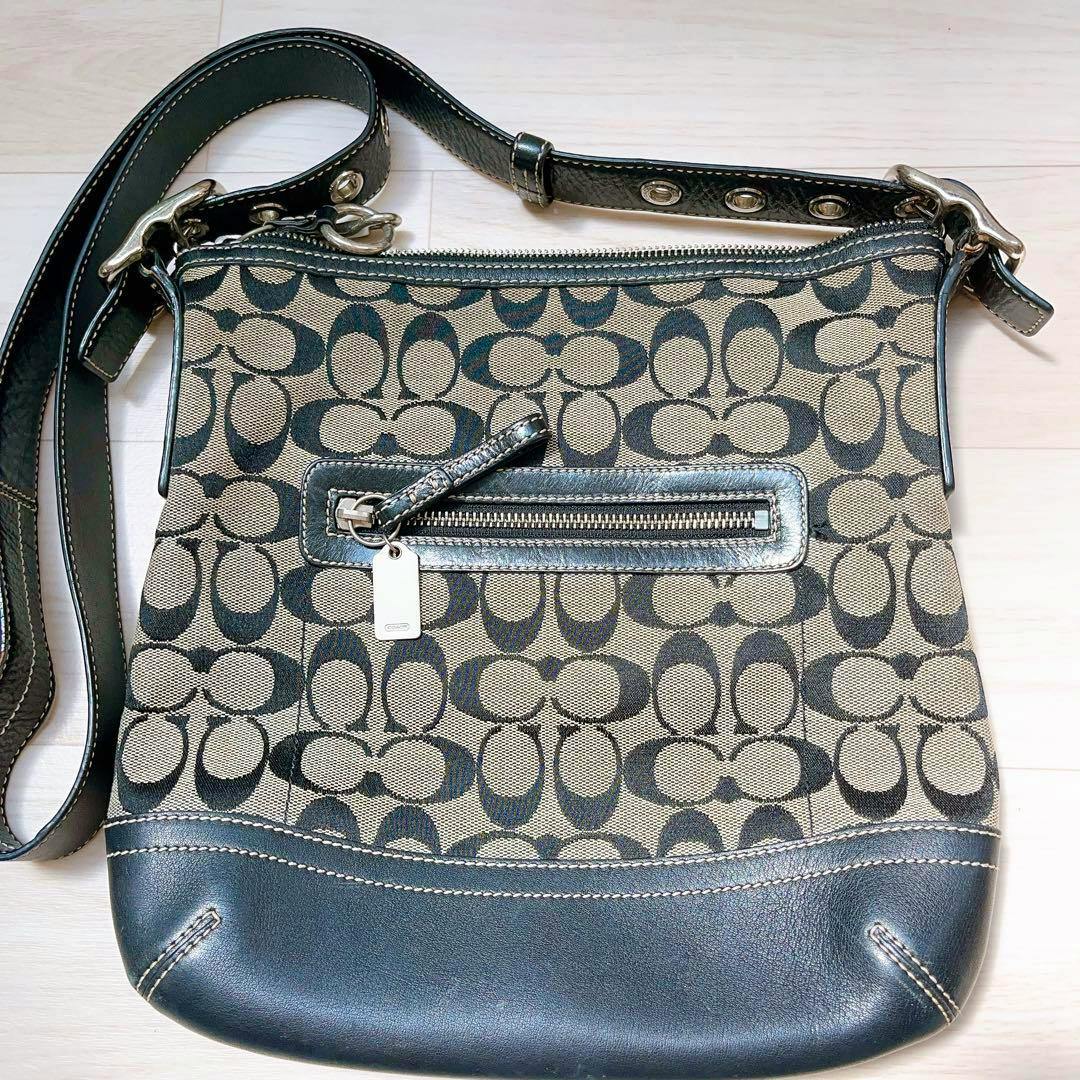 Front view of a COACH canvas shoulder bag showing the signature C pattern, front zip pocket, leather trim, and adjustable strap.