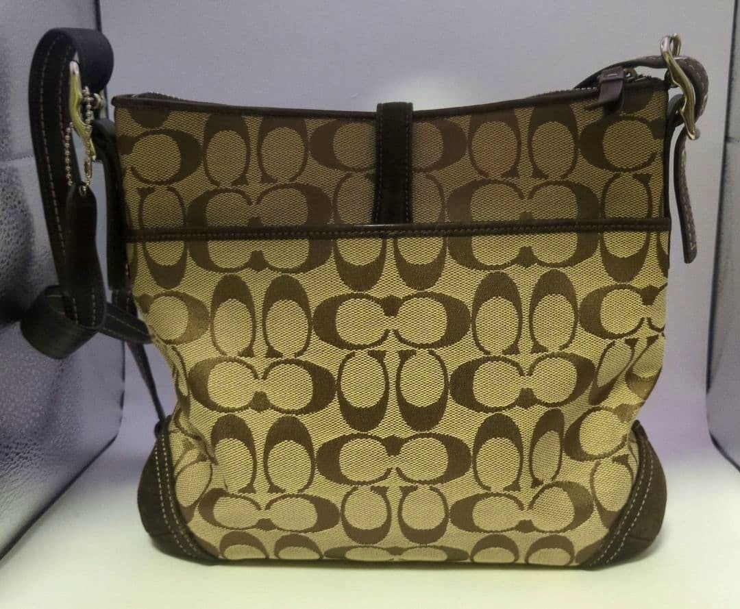Front view of a Coach canvas shoulder bag with brown signature 'C' pattern and brown leather trim.