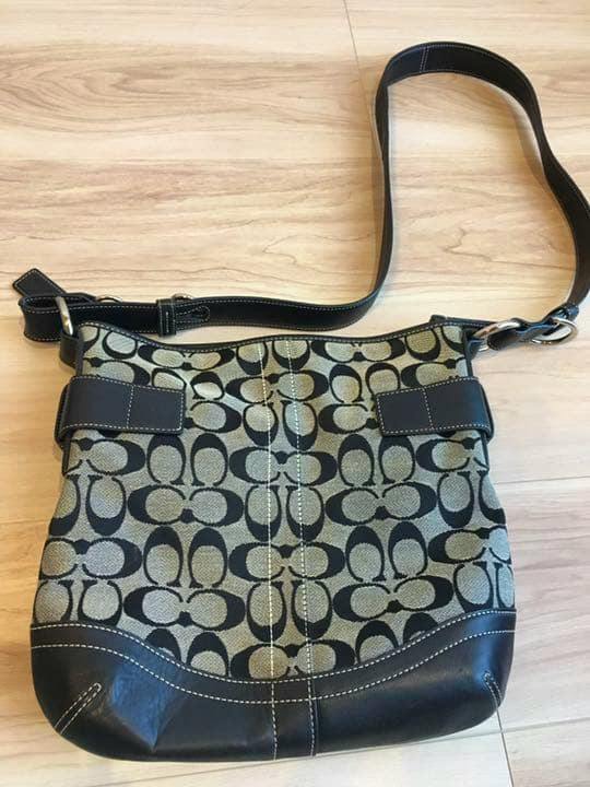 Front view of a COACH canvas shoulder bag with signature C pattern, leather trim, and an adjustable shoulder strap.