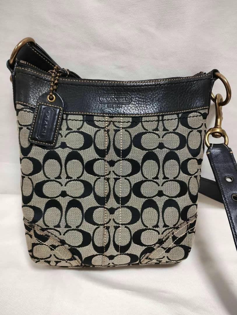 Front view of a Coach black canvas shoulder bag with signature C pattern, leather trim, and shoulder strap.