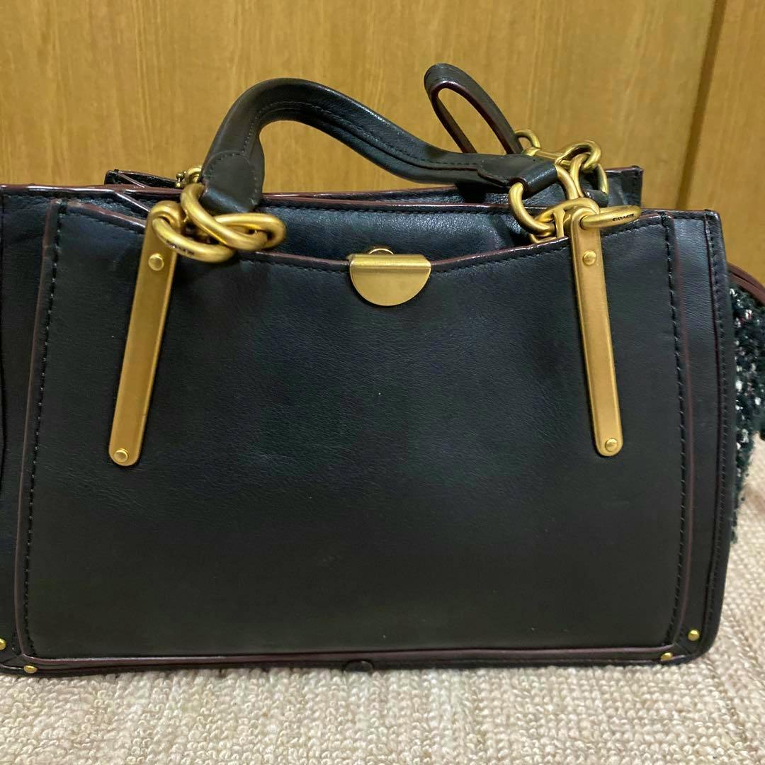 Front view of the Coach shoulder bag showing its black exterior, top handles, and gold metal hardware.