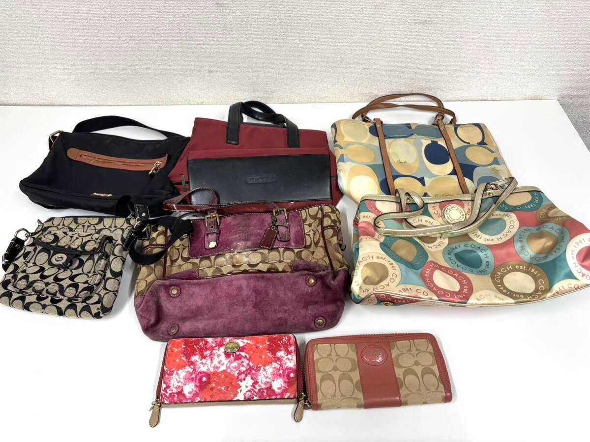 Multiple Coach canvas and leather handbags with two long wallets arranged on a white surface.