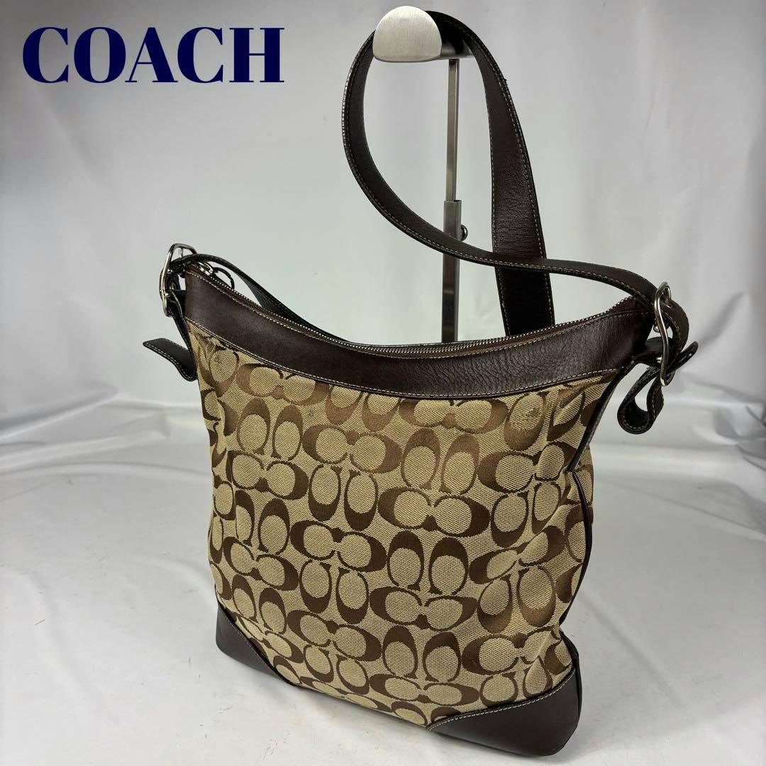 Dark brown COACH canvas signature shoulder bag with leather trim and strap displayed on a stand at a three-quarter angle.