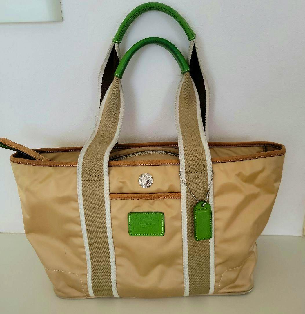 Beige COACH canvas tote bag with green leather top handles, beige webbing straps, front pocket, and a green leather tag.