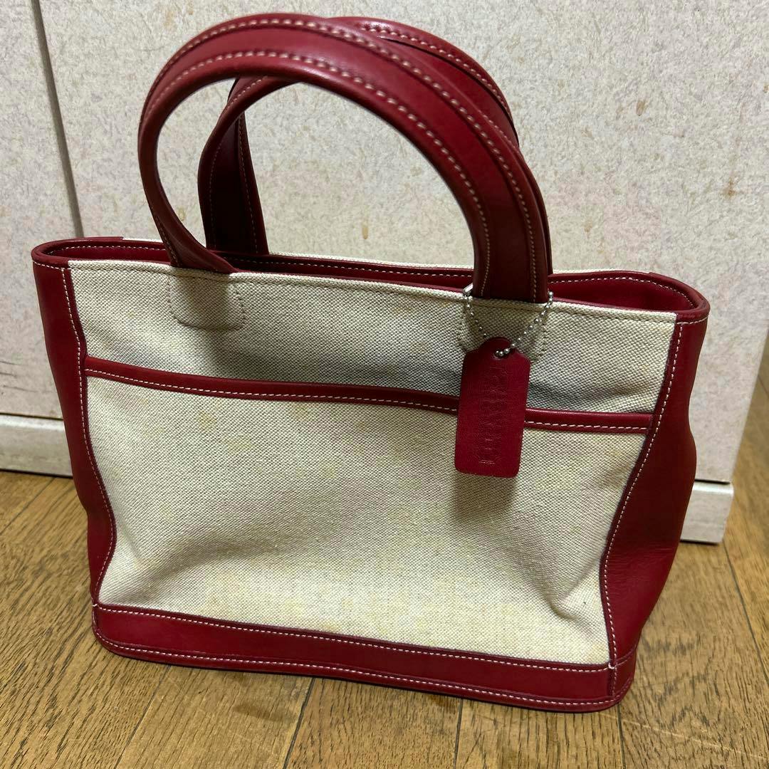 Red and white COACH canvas tote bag with red trim and double handles sitting on a wooden floor.