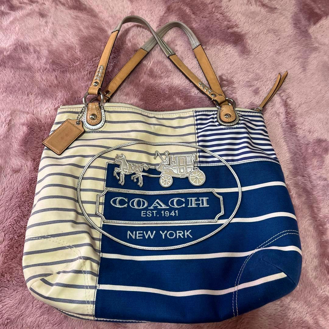 Canvas COACH tote bag with navy and cream stripes, leather handles, and a COACH New York logo patch visible on the front.