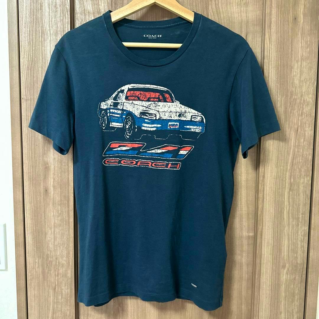 Navy cotton COACH T-shirt with a car graphic on the front hanging on a wooden hanger.