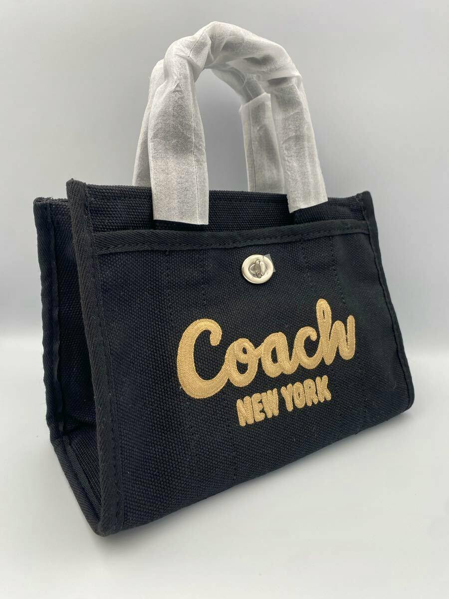 Black COACH tote bag with "Coach New York" gold lettering and wrapped handles on a plain light background.