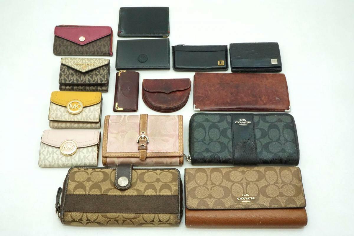 Assorted branded wallets and small leather cases laid out on a white background, including visible Coach patterned wallets.