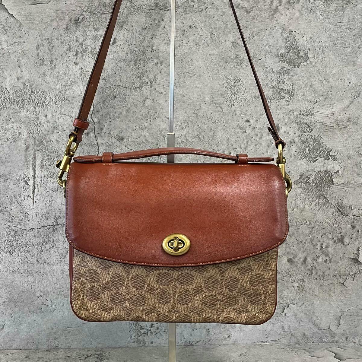 Front view of a brown Coach 2-way shoulder bag with signature canvas lower, leather flap, top handle, adjustable strap, and turnlock closure.
